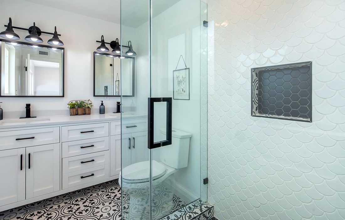 A bathroom with a patterned tile floor, a double vanity and a glass shower