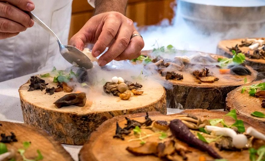 A cook plating small dishes on wooden boards with steam rising